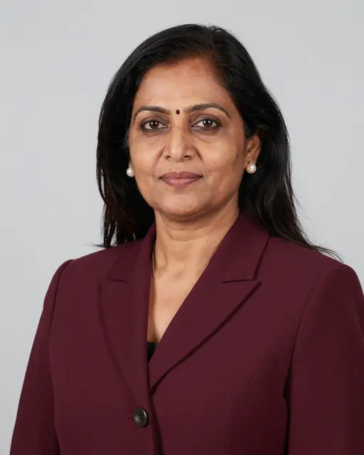 Head and shoulders studio portrait of a middle-aged South Asian woman in a maroon blazer with pearl earrings