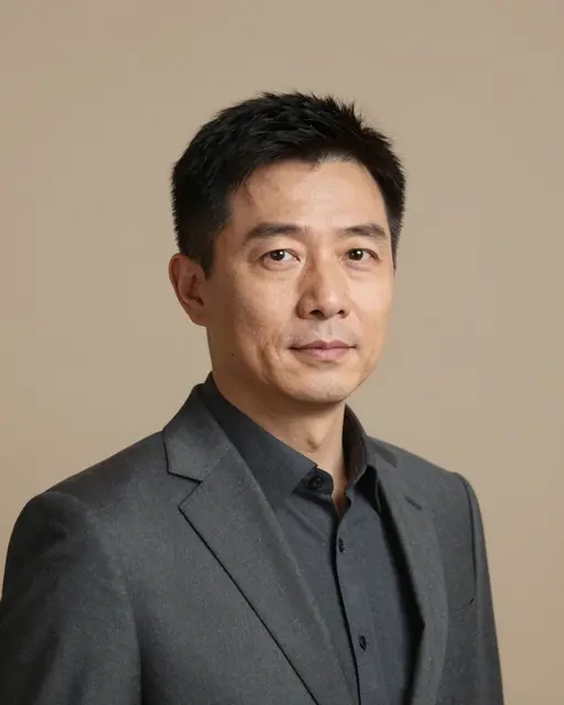 Studio headshot of a middle aged East Asian man in a charcoal suit against a taupe backdrop