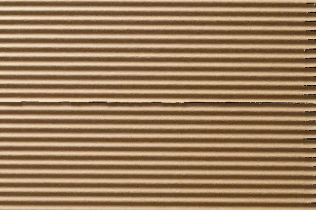 Full frame top view of exposed brown corrugated cardboard with parallel fluted ridges