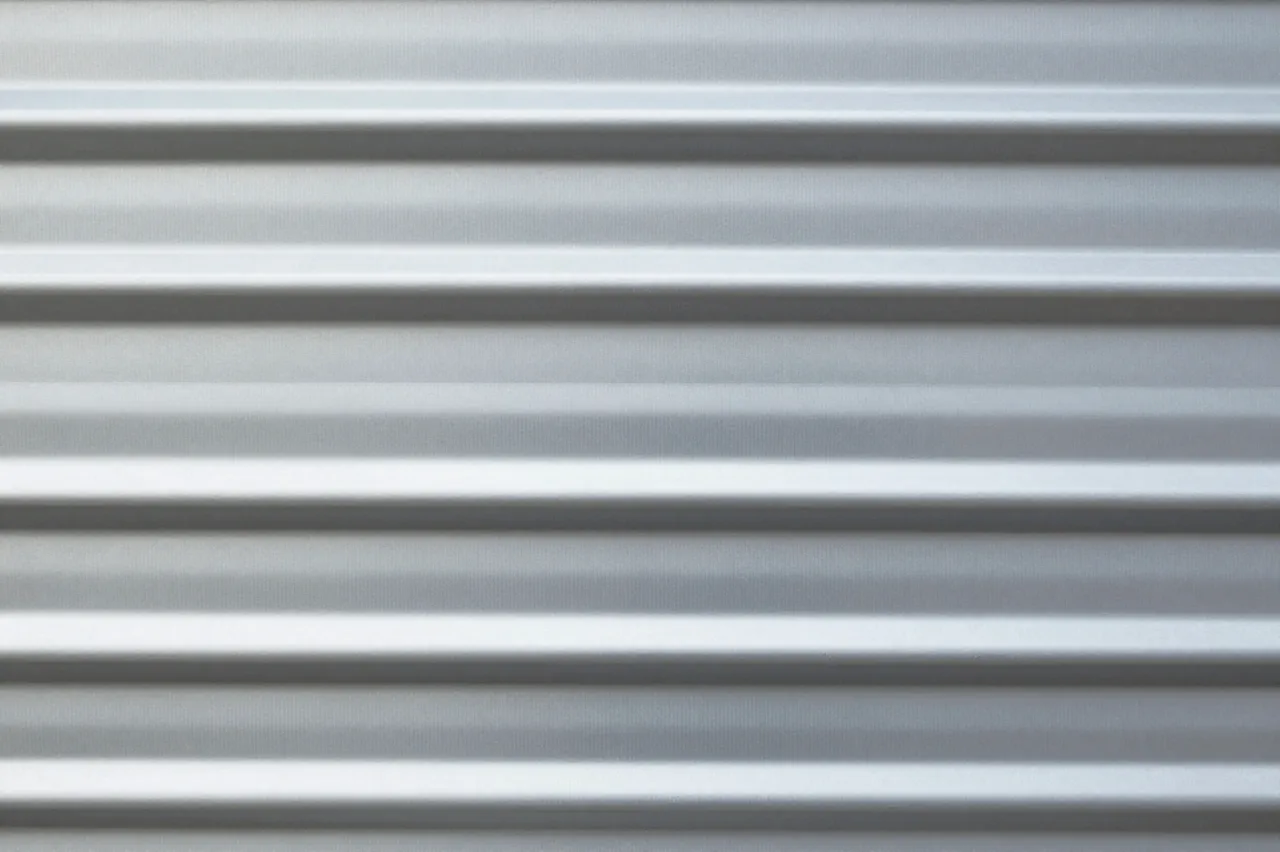 Close-up horizontal view of a smooth gray corrugated metal sheet with alternating light and shadow ridges
