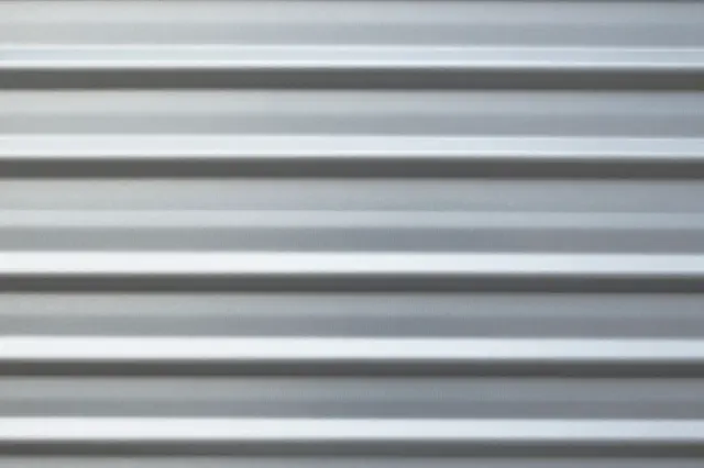 Close-up horizontal view of a smooth gray corrugated metal sheet with alternating light and shadow ridges