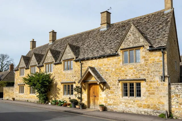 Row of honey-colored stone Cotswolds cottages lining a quiet village street under pale clear sky