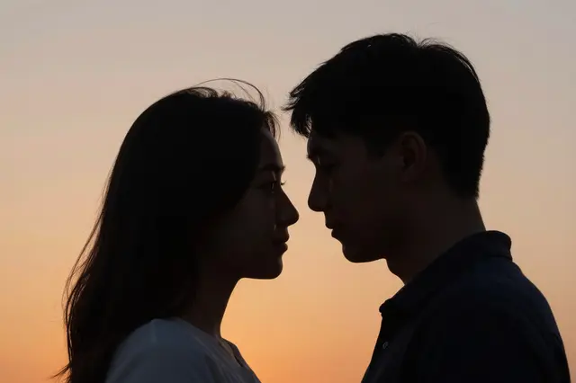 A man and woman stand face to face against a soft gradient orange sunset sky.