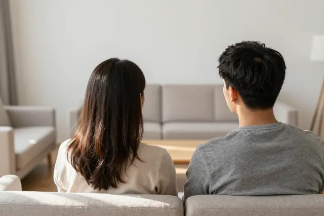 A couple seen from behind sits looking out at a bright unfurnished living room space.