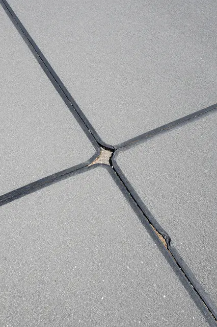 Top view of faded gray asphalt with crossing cracked black tar sealant lines