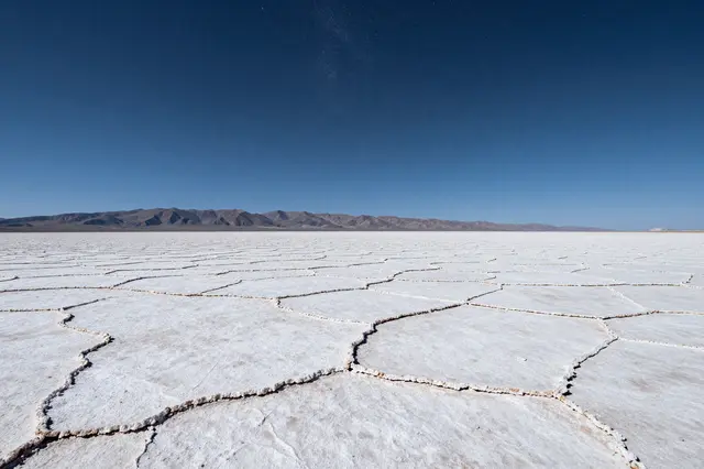 Cracked white salt flat stretches toward distant mountains under a deep blue clear sky