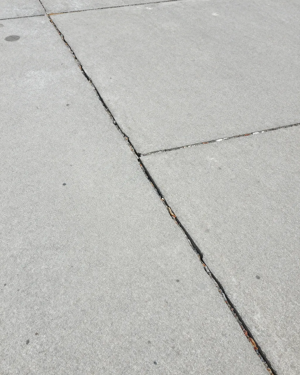 Top view of light gray cracked concrete pavement with slab joints and faint surface stains.
