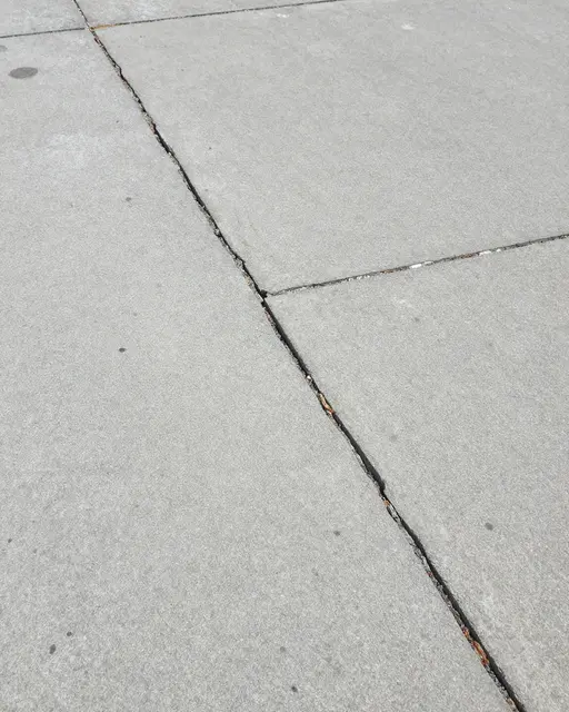 Top view of light gray cracked concrete pavement with slab joints and faint surface stains.