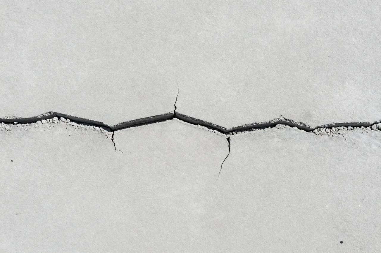 Top view of a flat light gray concrete surface crossed by a wide jagged horizontal crack with chipped edges