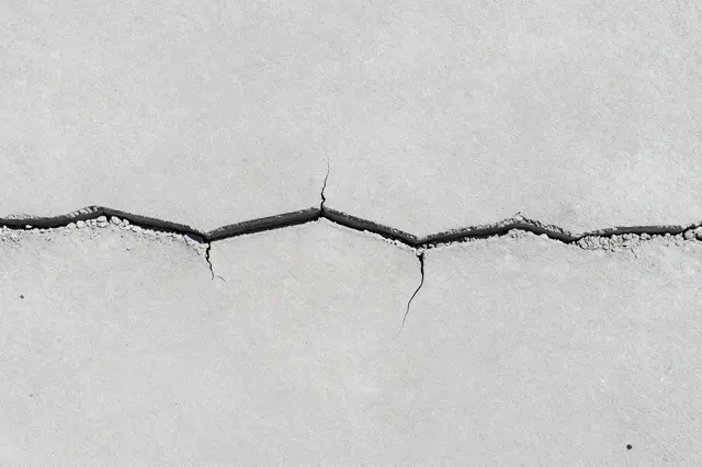 Top view of a flat light gray concrete surface crossed by a wide jagged horizontal crack with chipped edges