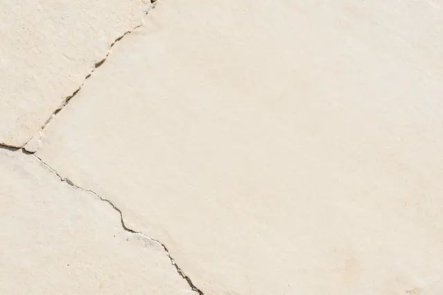 Full frame close-up of pale cream limestone with natural cracks and a rough matte surface