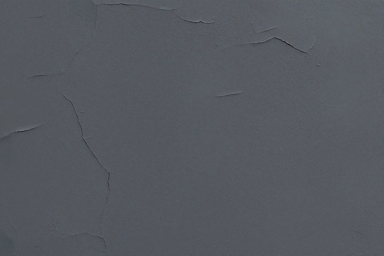 Full frame close-up of weathered dark gray plaster with fine uneven cracks across its surface
