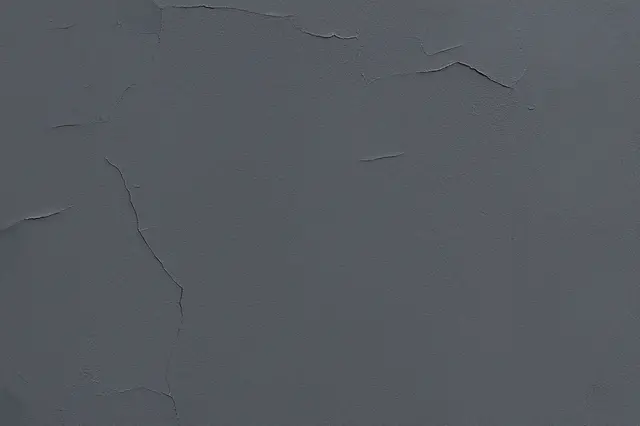 Full frame close-up of weathered dark gray plaster with fine uneven cracks across its surface