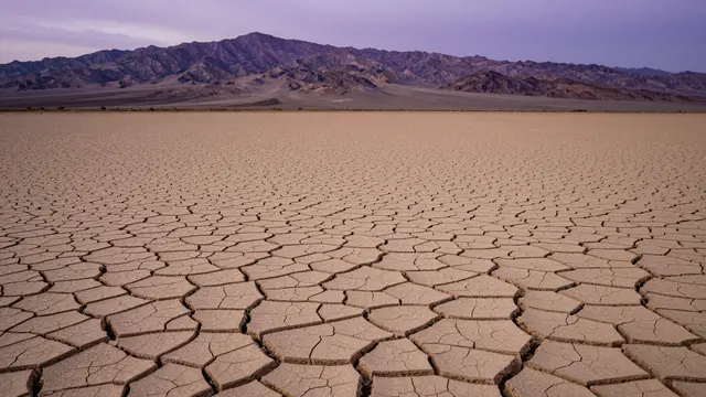 Cracked dry desert clay stretches to distant purple mountains under a dusky purple sky