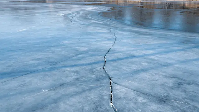 Wide view of cracked melting pond ice with open reflective water at the edge under bright spring sun