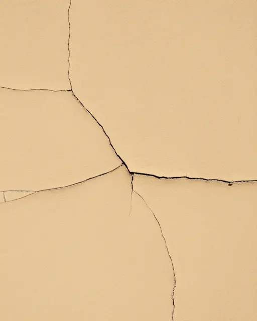 Full frame close-up of weathered ochre plaster marked by dark branching crazing cracks under flat even light