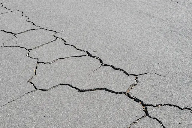 Top view of sun-bleached gray asphalt covered in a web of intersecting cracks filling the full frame
