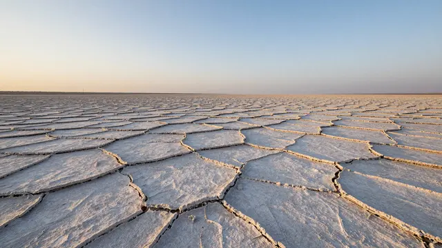 Geometric cracked salt crust stretches across an empty flat toward the horizon under a soft gradient dusk sky