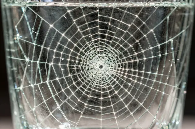 Close-up of crackle glass showing a web of fine glowing internal fractures across its surface