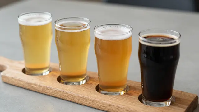Four beer glasses of varying shade from pale gold to dark stout rest on a wooden flight board