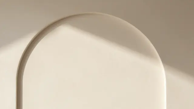 Soft diagonal sunlight falls across a smooth cream plaster wall with a rounded architectural arch detail