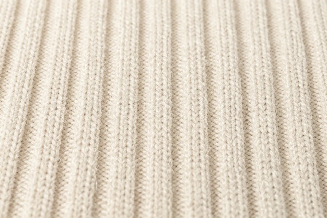 Close-up view of soft cream ribbed knitted wool fabric texture