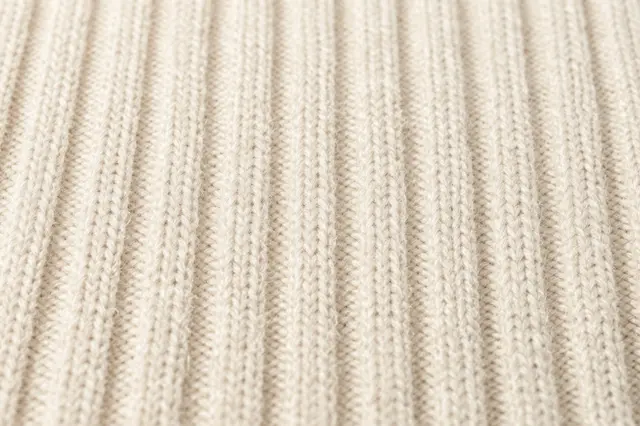 Close-up view of soft cream ribbed knitted wool fabric texture