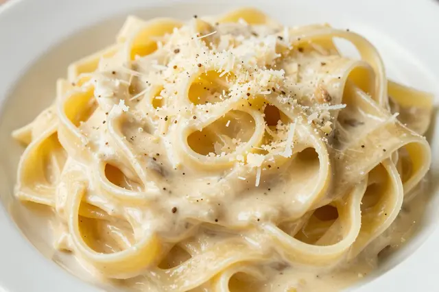 Close-up view of creamy fettuccine alfredo topped with grated parmesan and black pepper in a white bowl