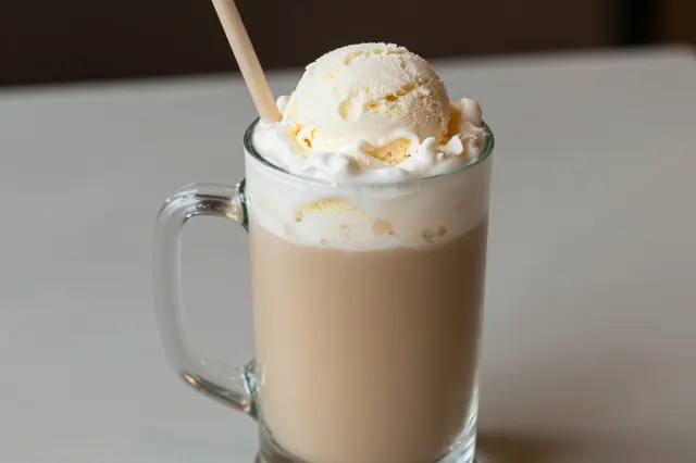 A frosty glass mug holding a root beer float topped with vanilla ice cream and a wooden straw.