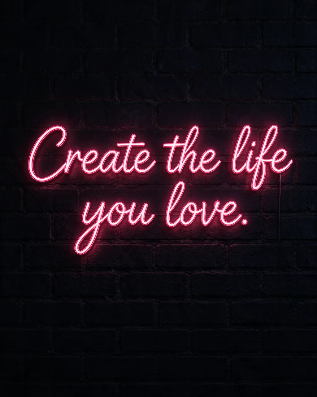 Glowing pink neon sign reading "Create the life you love." mounted on a dark brick wall at night