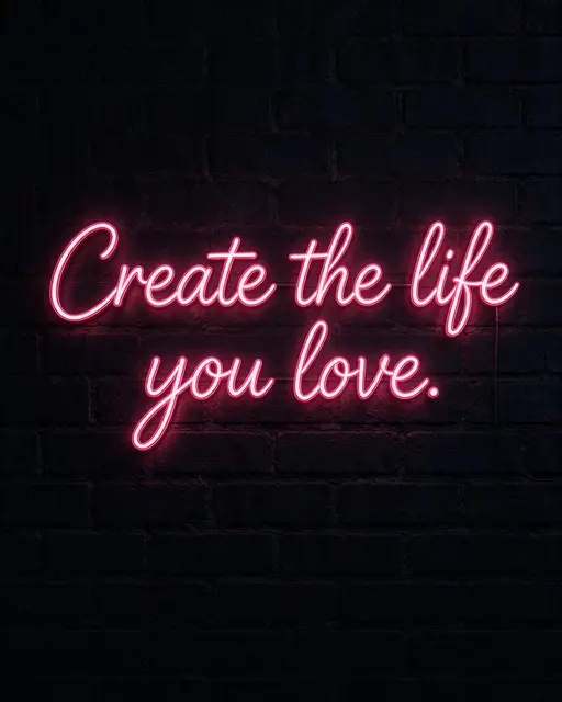 Glowing pink neon sign reading "Create the life you love." mounted on a dark brick wall at night