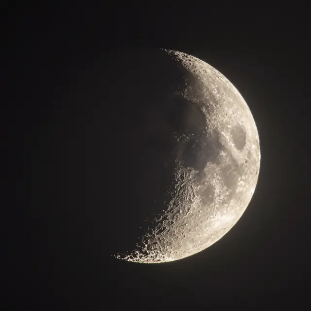 Telescope view of a thin crescent moon showing cratered surface details against dark night sky