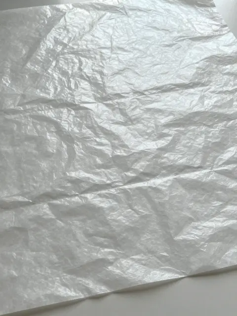 A close-up of crinkled translucent glassine paper with a soft waxy sheen under even overhead lighting