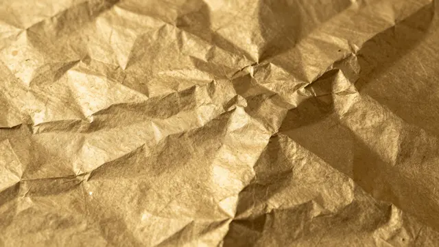 Close-up view of crinkled warm gold foil catching soft warm light across its textured creased surface