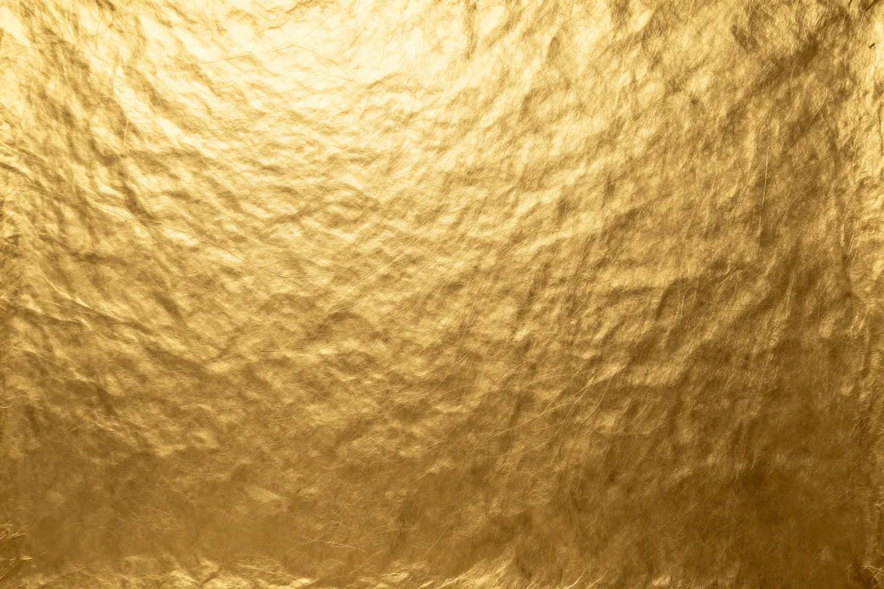 Full frame close-up of crinkled warm gold foil surface with soft even light reflections
