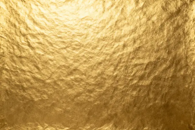 Full frame close-up of crinkled warm gold foil surface with soft even light reflections