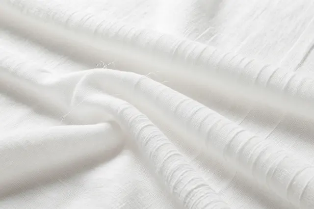 Close up of crinkled layered off-white cotton gauze fabric with soft even lighting and loose threads