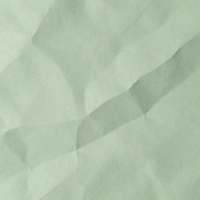 Full frame close up of smoothed crinkled sage green paper with soft highlights along its creases