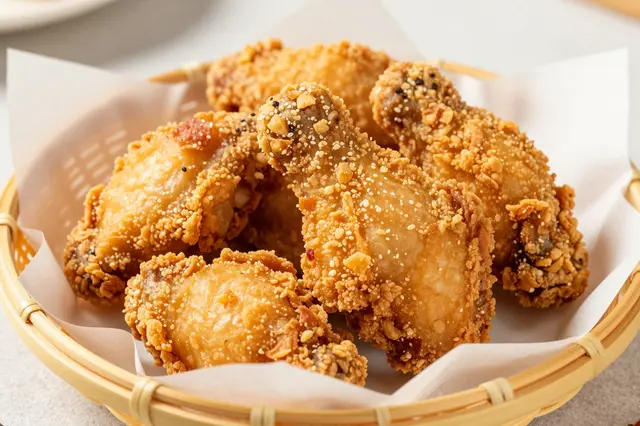 Crispy breaded fried chicken pieces sit in a parchment-lined woven bamboo basket on a light countertop