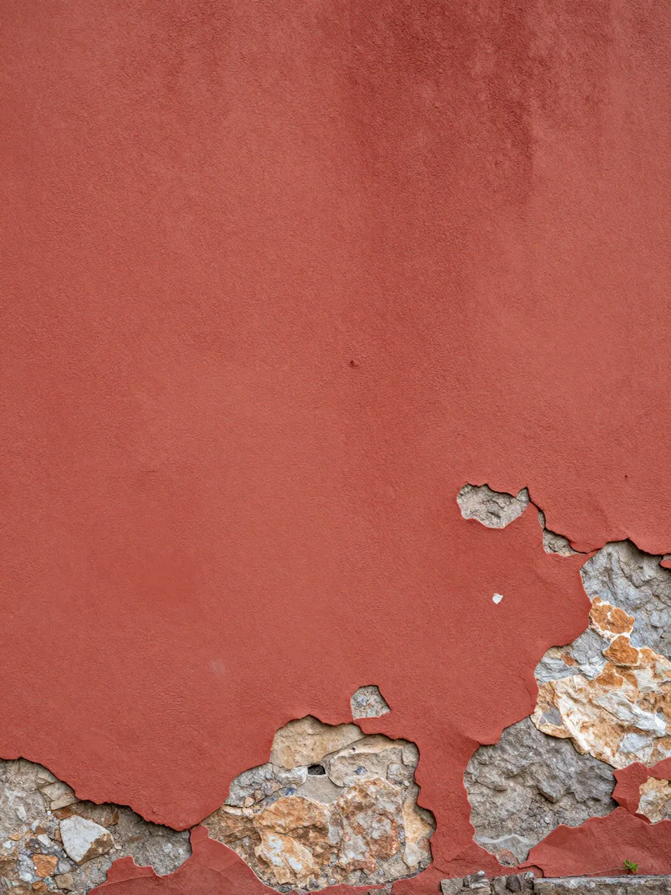 Weathered red plaster wall peeling away to reveal rough underlying stone rubble