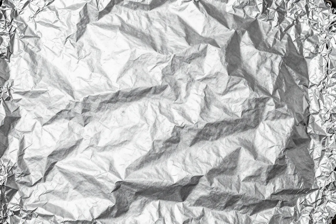 Full frame close-up of heavily crumpled reflective silver aluminum foil surface