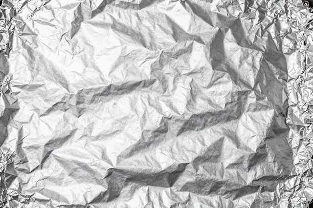 Full frame close-up of heavily crumpled reflective silver aluminum foil surface