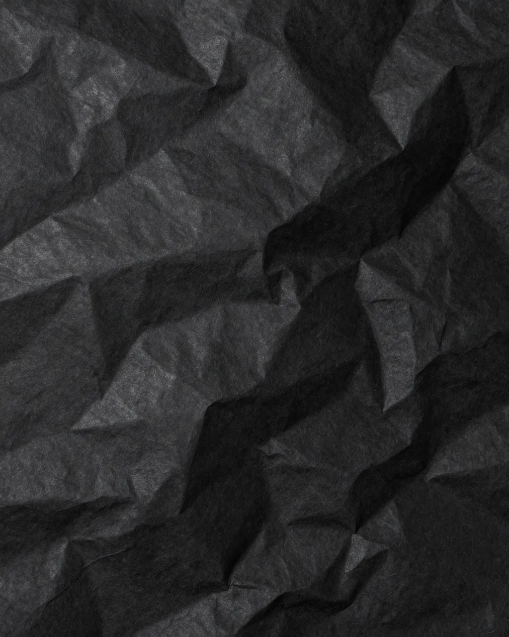 Full frame close-up of crumpled black paper with subtle sheen on raised ridges