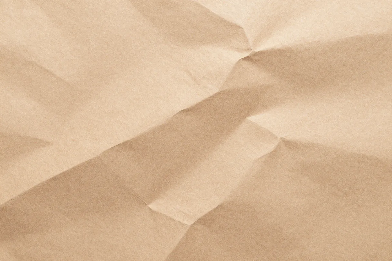 Full frame close-up of crumpled light brown kraft wrapping paper with sharp folded creases