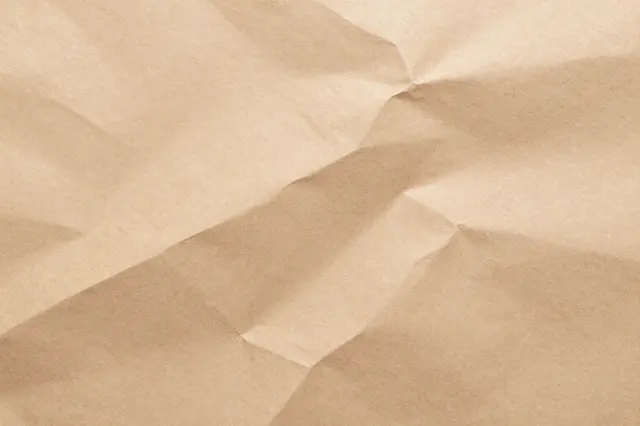 Full frame close-up of crumpled light brown kraft wrapping paper with sharp folded creases