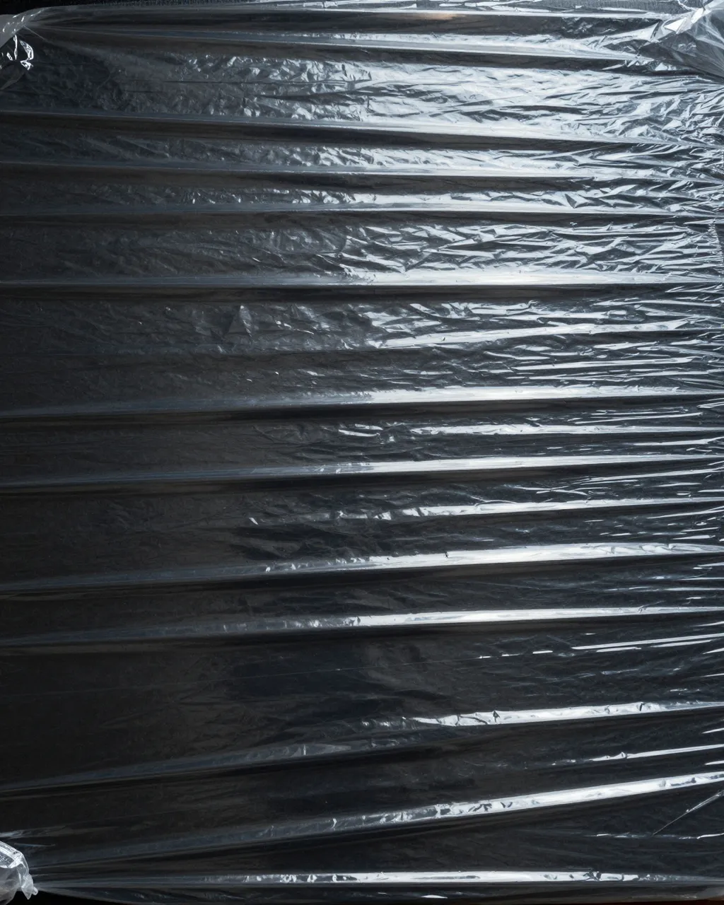 Full frame close-up of crumpled glossy clear plastic wrap stretched over a solid black background with bright wrinkle