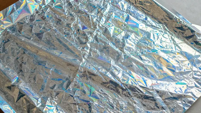 Close-up of crumpled iridescent holographic foil with shifting rainbow light reflections across its wrinkled surface