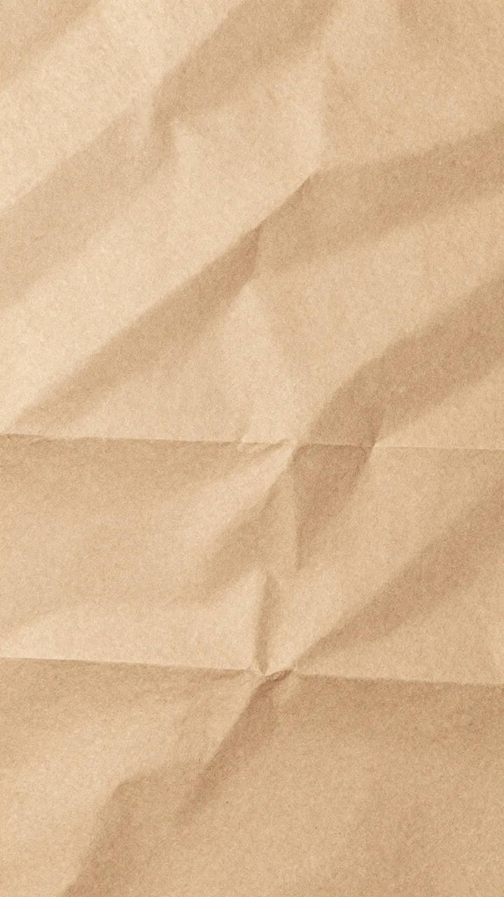 Full frame vertical close up of crumpled natural kraft paper with soft warm lighting along deep folded creases