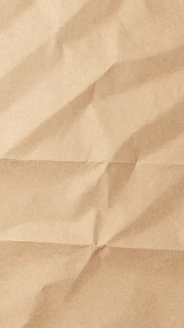 Full frame vertical close up of crumpled natural kraft paper with soft warm lighting along deep folded creases