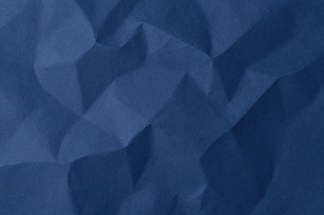 Full frame close-up of crumpled navy blue paper with soft highlights along folded ridges